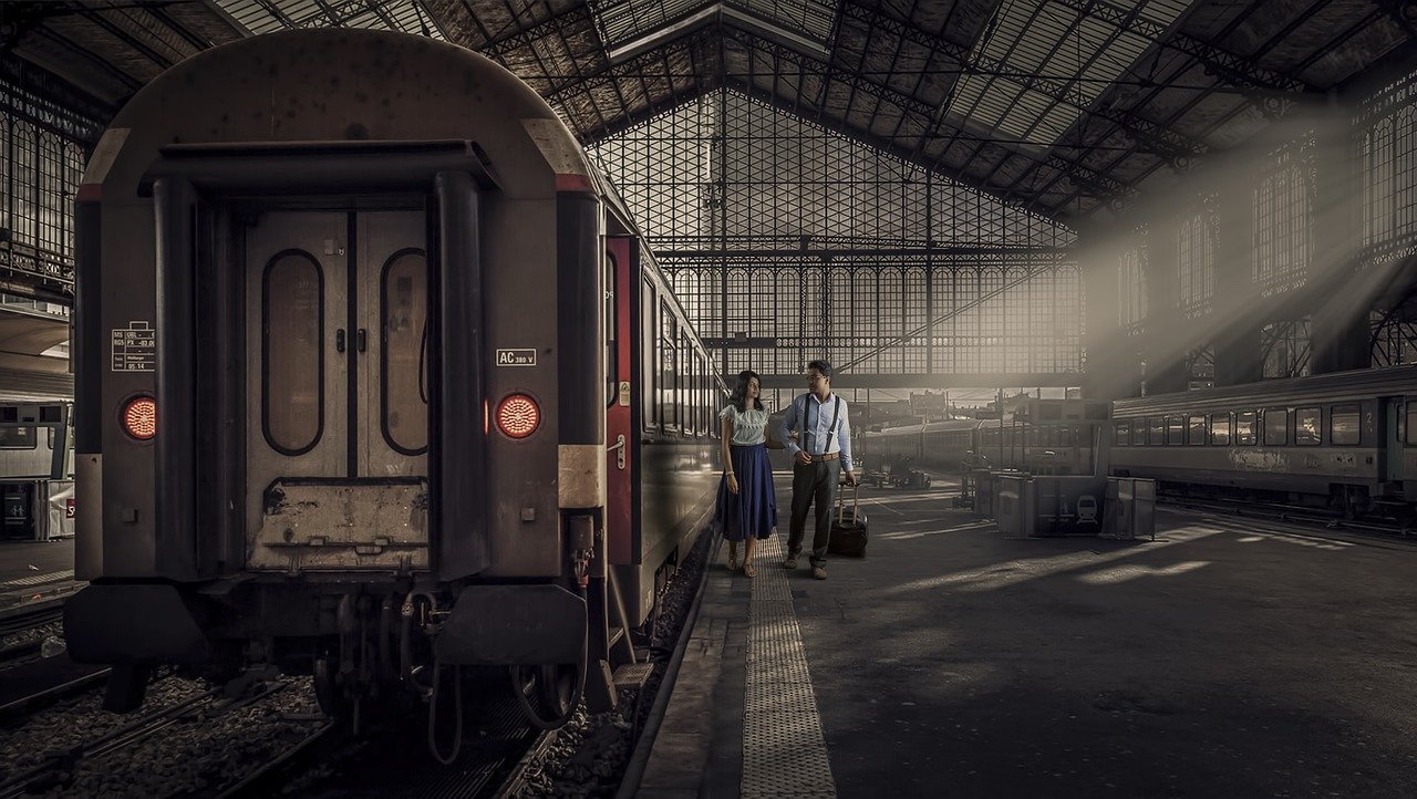 To personer med bagasje går ved et tog inne på en stasjon
